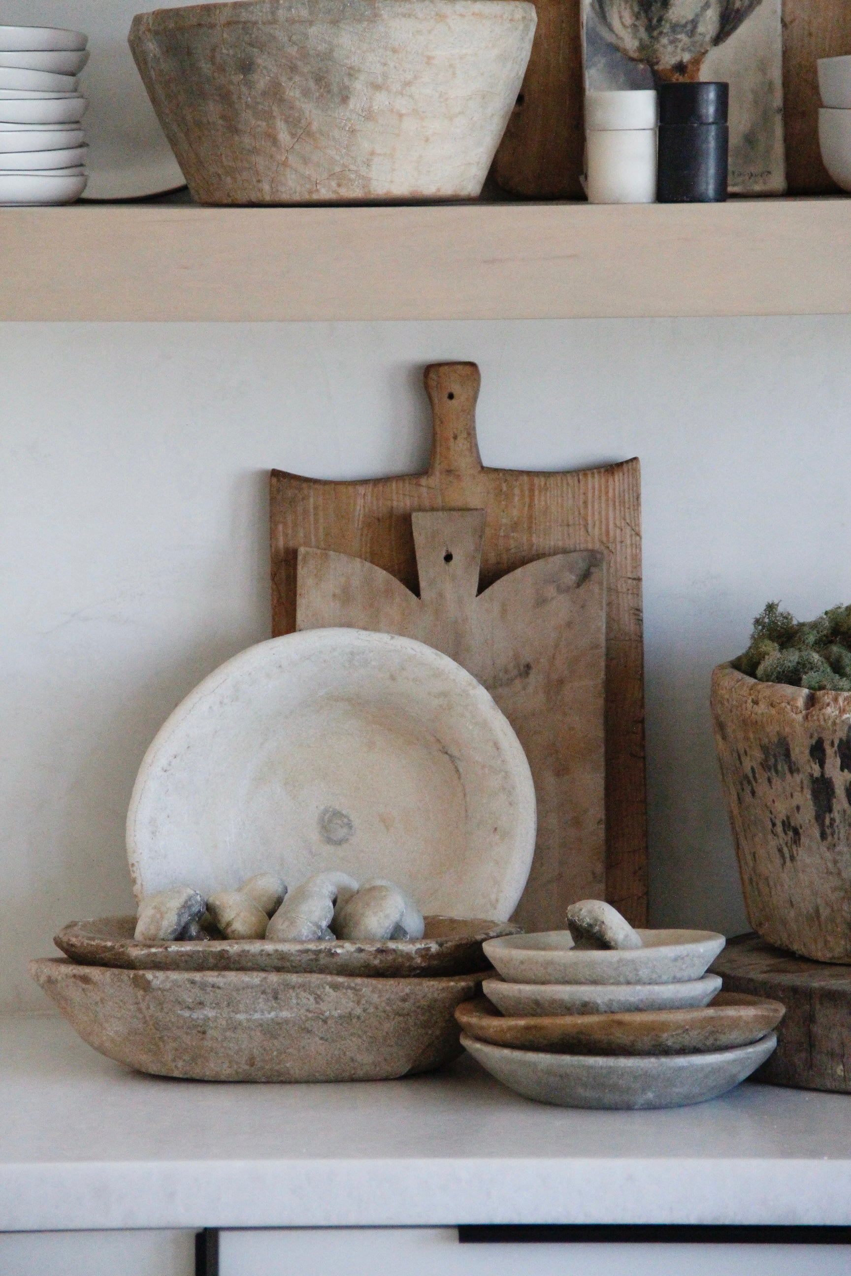 Collection of rustic kitchenware including bowls and a cutting board on a shelf.